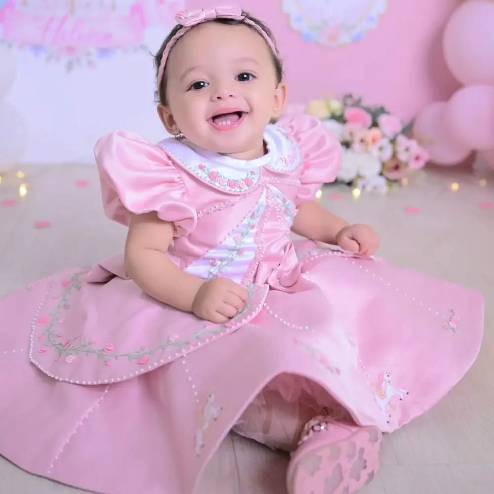 Bebê sorrindo com vestido rosa bordado no primeiro aniversário