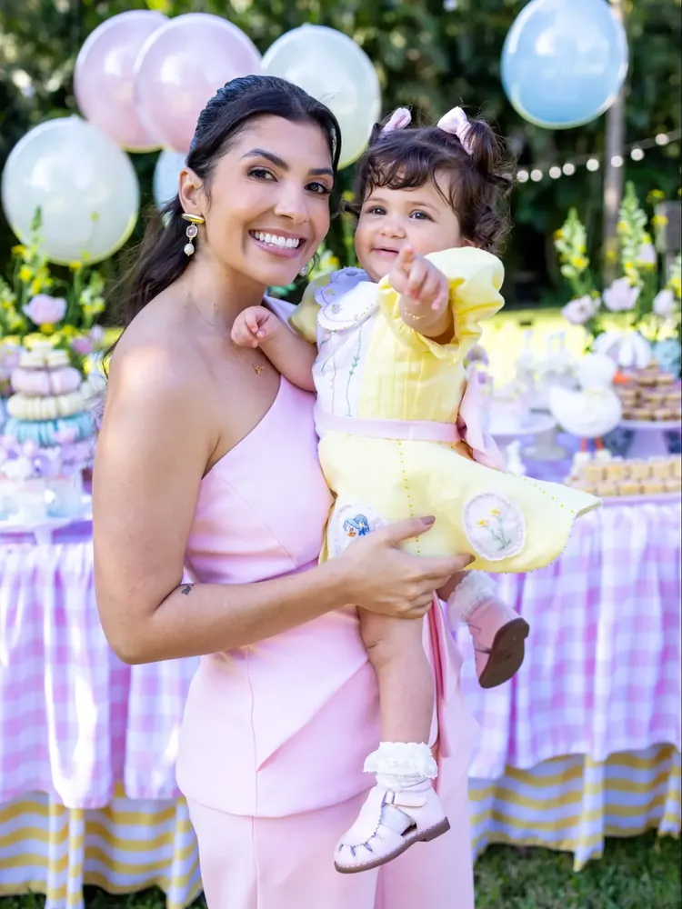 Mãe segurando a filha com vestido amarelo bordado à mão